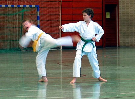 Zwei Kinder beim Karatetraining. Einer greift mit einem Fauststoß an, der andere kontert kontaktlos mit einem Fußtritt.
